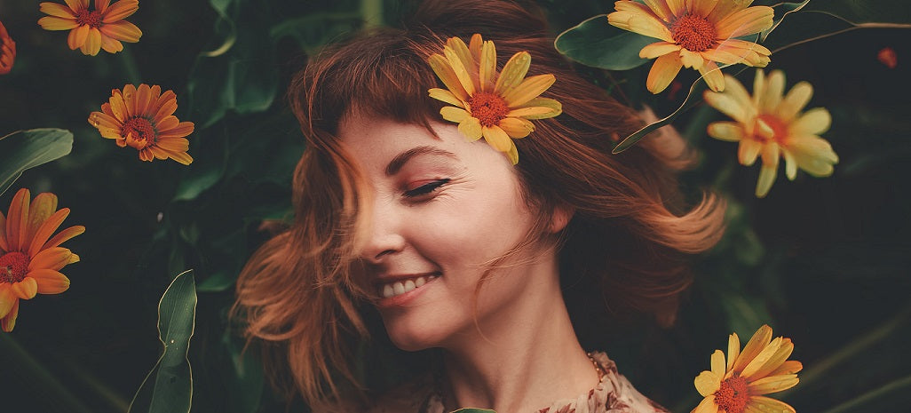 Smiling woman with orange gerbera daisies in her hair surrounded by flowers